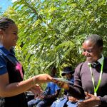 Leya Mnangagwa hands a book to a smiling student at a community visit, an example of purposeful business leadership in action.